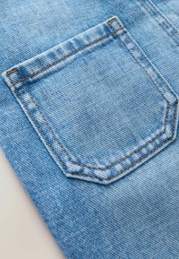 Ljust blå denimtyg med en hexagonal bakficka med kontrasterande brun sömnad och en subtil textur.