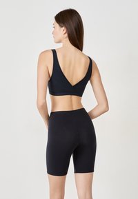 Schwarzer nahtloser BH mit einem V-Rücken-Design, kombiniert mit Shorts bis zur Mitte des Oberschenkels, beide aus glattem, dehnbarem Material gefertigt.
