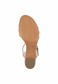 Sandale beige avec une tige semi-transparente, une bride ajustable à la cheville, un talon plat et rond, et une semelle en caoutchouc texturée avec des rainures horizontales.