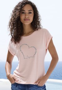Heledad roosa lühikeste varrukatega T-särk, millel on hõbedane südamekujuline disain ja sõna "Lovely" allpool, valmistatud pehmest ja siledast kangast.