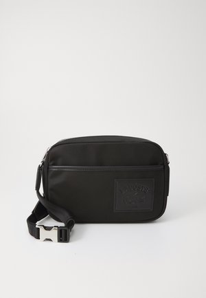 Black nylon crossbody bag with a textured logo patch, zip closure, and adjustable strap featuring a silver-tone clasp.