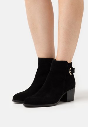 Schwarze Wildleder-Stiefeletten mit einem Blockabsatz, die über eine seitliche Schnallenakzentuierung und ein elegantes, schnittiges Design verfügen. Glatte Textur mit gebogenem Schaft.