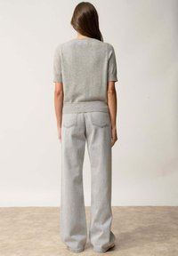 Szary sweter z krótkim rękawem wykonany z dzianiny, zestawiony z jasnoszarymi spodniami o szerokich nogawkach. Miękka tekstura, luźny krój oraz widoczne szwy tylnej kieszeni.