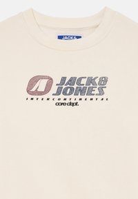 T-shirt in cotone color crema con stampa grafica in blu scuro e rosso, riportante il testo "JACK & JONES INTERCONTINENTAL core dept."