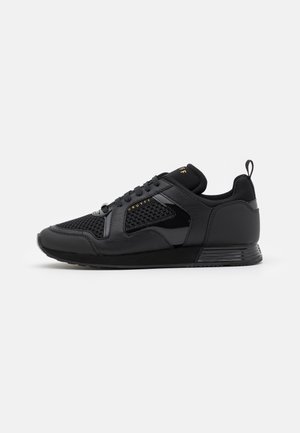 Chaussures de sport noires avec une tige en mesh, des accents en cuir lisse, des lacets plats et une semelle texturée. Dotées d'une languette au talon.
