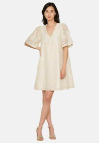 Kerge koorevärvi A-lõikega kleit pitskattega, V-avaga ja lühikeste puhvärvidega. Kandmiseks metallikist rihmadega sandaalid.