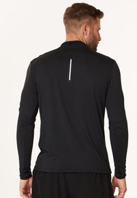Sort langærmet træningsshirt med en glat tekstur, der har en reflekterende vertikal stribe på ryggen og en tætsiddende pasform omkring håndleddene.