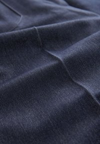 Tissu en denim bleu foncé avec un motif de tissage diagonal visible et des plis subtils sous un éclairage doux.