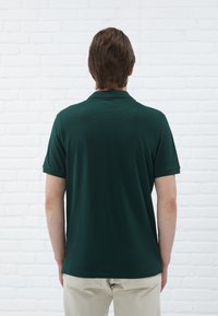 Polo shirt vert foncé à manches courtes, avec un col et une coupe décontractée. Texture lisse avec fentes sur les côtés à l'ourlet.