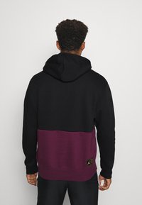 Sweat à capuche noir et marron avec un design bicolore, doté d'une capuche à cordon de serrage et d'un écusson logo à l'ourlet. Tissu doux, coupe décontractée.