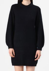 Robe pull noire en tricot avec un col rond et de longues manches bouffantes ajustées. La texture est douce et légèrement duveteuse.