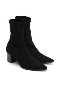 Bottines noires avec un tissu doux et extensible et un bout pointu. Caractérisées par un talon carré épais et des coutures décoratives sur les côtés.