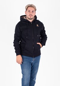 Felpa nera con zip e fodera interna a scacchi, con stringhe regolabili e tasche frontali, abbinata a jeans di denim blu.
