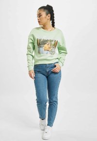 Mintgrønn genser med trykt grafikk av en jente i et uformelt antrekk, sammen med lyseblå skinny jeans og hvite sneakers.