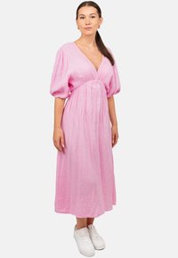 Roze, jurk tot de knie met een v-hals, losse pofmouwen, textuurstof en een gathered taille, gecombineerd met witte sneakers.