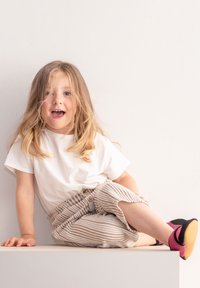 Weißes T-Shirt mit kurzen Ärmeln, leichte gestreifte Hose mit elastischem Bund und schwarz-pinke Schuhe mit strukturierten Sohlen.