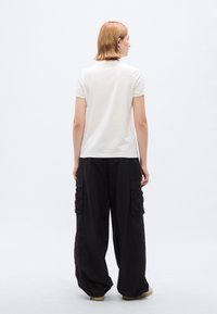 Λευκό κοντομάνικο μπλουζάκι συνδυασμένο με φαρδιά μαύρη παντελόνα cargo με πολλαπλές τσέπες, φορεμένο με ανοιχτόχρωμα παπούτσια.