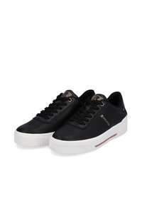 Baskets en cuir noir avec semelle en caoutchouc blanche, comportant des perforations décoratives, des lacets plats et des accents métalliques sur le côté.