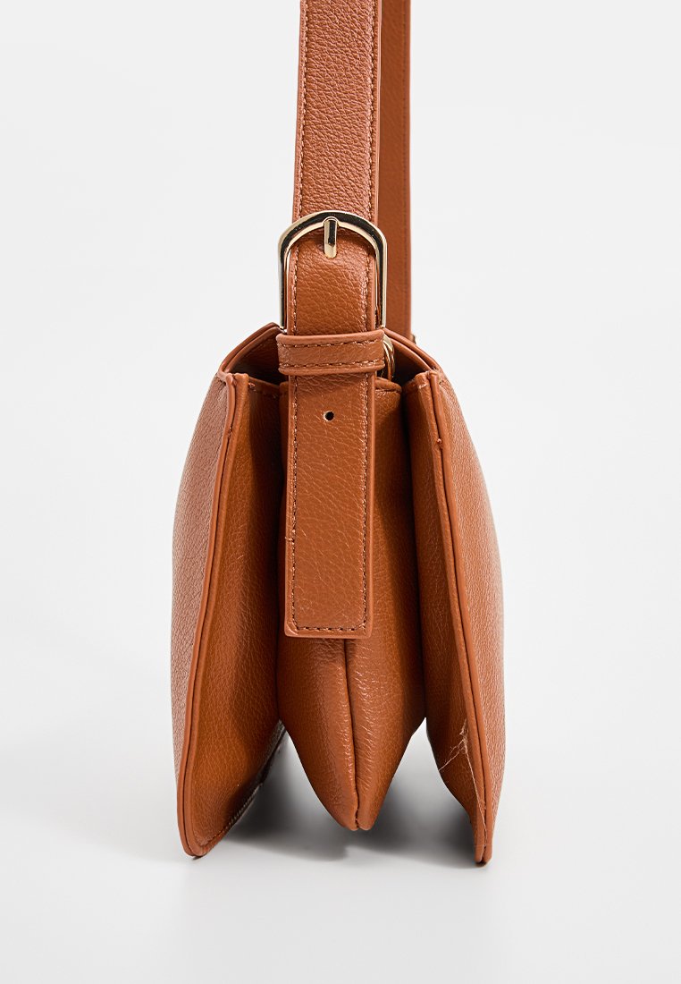 Sac en cuir marron texturé avec bandoulière réglable et boucle dorée, vu de côté avec trois compartiments visibles.