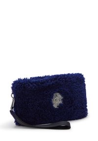 Bolso de mano de felpa azul marino con un emblema de estrella metálica circular y una correa de muñeca negra desmontable sobre un fondo blanco.