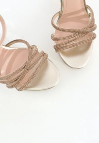 Sandales à talons hauts métalliques dorées avec de multiples bandes croisées ornées de petits rhinestones marron, présentant une surface lisse et brillante.