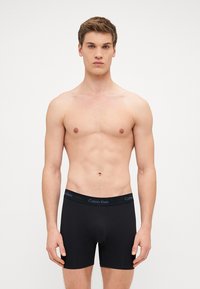 Fekete pamut boxer alsónadrág logóval ellátott derékpánttal. Az anyag simának tűnik, testhezálló fazonú és középmagas derékú.