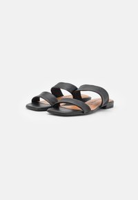 Ett par svarta platta sandaler med två breda vadderade remmar och en fyrkantig öppen tå på en vit bakgrund.