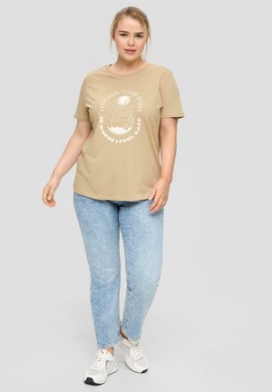 Beige katoenen T-shirt met korte mouwen, voorzien van witte grafische tekst en illustraties. Gepaard met lichtblauwe spijkerbroeken en witte sneakers.