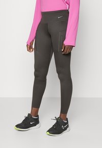 Leggings de carbón con una cintura alta y bolsillos con cremallera, combinados con una camiseta de manga larga rosa y zapatillas de correr negras con acentos de neón.