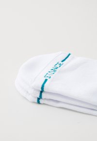 White socks with a reinforced toe, featuring a turquoise stripe and “STANCE” embroidered on the side. Made of soft, textured material.