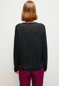 Tummanharmaa, pitkähihainen neulepaita, jossa on rento istuvuus ja pyöreä pääntie. Kangas vaikuttaa pehmeältä ja hienorakeiselta.