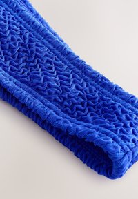 Kék, texturált szövetszalag fodros mintával, sima szegéllyel. Különféle redőket tartalmaz a térhatás érdekében.