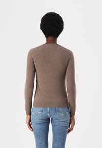 Maglione marrone, strutturato, con maniche lunghe e scollo rotondo, abbinato a jeans in denim blu. Vista da dietro.