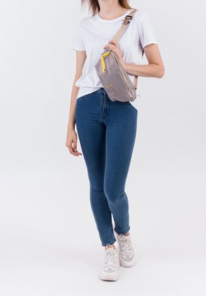 Grijze tas met een textuurpatroon, gele ritstrekker en verstelbare riem, diagonaal gedragen over een wit T-shirt en blauwe spijkerbroek.