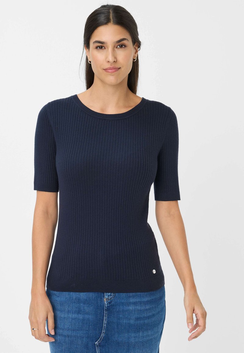 Marineblå ribbet strik top med korte ærmer, rund halsudskæring og lille logo detalje ved sømmen, parret med blå denim jeans.