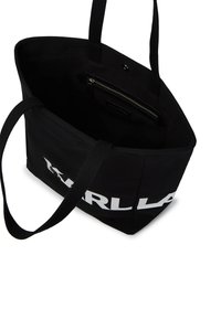 Fekete vászontáska fehér logóval. Tartós vállpántokkal rendelkezik, belső cipzáras zsebbel és tágas főrekesszel.