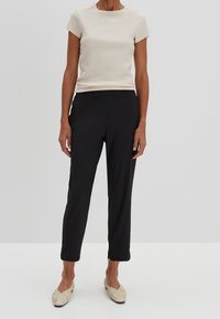 Ljust beige, ribbat kortärmad topp kombinerad med svarta skräddarsydda byxor och beige slip-on skor med ett subtilt lövmönster.