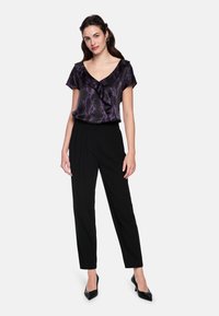 Black trousers paired with a purple and black snake-patterned blouse featuring a ruffled neckline. The ensemble is complemented by sparkly black heels.