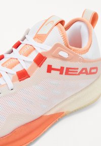 Head athletic shoe featuring a breathable white mesh upper with peach accents, prominent logo, and a textured orange sole for traction.