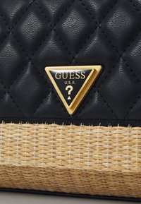 Borsa nera trapuntata con fondo in paglia intrecciata. Presenta una piastra con logo triangolare dorato, tessuto strutturato e materiali a contrasto.