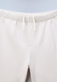 Close-up van een witte sweatpants met elastische tailleband, aantrekkoordjes en zichtbare voorste stiksel details.