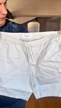 Pantalones cortos de tiro con cordón de color beige, hechos de tela ligera. Cuentan con una cinturilla elástica y bolsillos laterales. Etiqueta visible en la cintura.