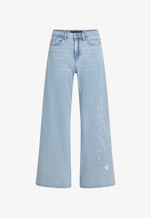 Jeans de perna larga azul claro em denim com texto costurado "Donald e Daisy" na perna esquerda. Apresenta um design clássico de cinco bolsos e passantes para cinto.