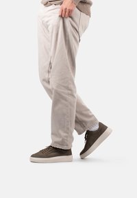 Baskets en cuir marron foncé avec bout arrondi, surface texturée et semelle claire contrastante. Portées avec un pantalon beige clair à coupe ample.