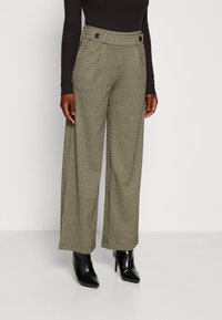 Pantalon taille haute à jambes larges avec un motif pied-de-poule en noir et crème, doté de boutons décoratifs et d'un tissu texturé.