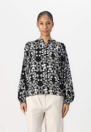 Svart og hvit blomstermønstret bluse med bandkrage og lange ermer, med rynkede mansjetter og en løs passform.