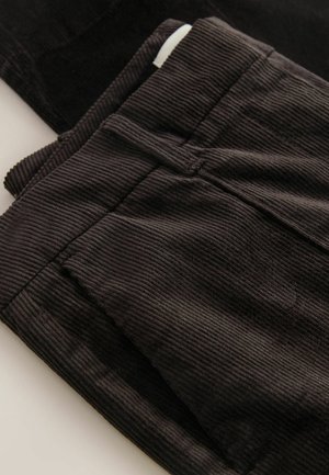 Schwarzer Cordstoff mit vertikalen Rippungen, ausgestattet mit Taschen und einem Bund, der ein strukturiertes Erscheinungsbild bietet.