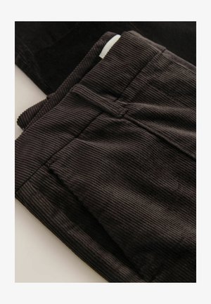 Tessuto di corduroy nero con rigature verticali, dotato di tasche e una cintura, che presenta un aspetto testurizzato.