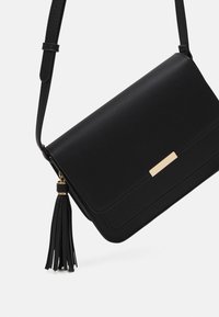 Borsa a tracolla nera in pelle con accentuazione dorata e nappina. Presenta una forma rettangolare e una texture liscia. Include una tracolla regolabile.