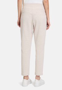 Beige, strukturierte Hose mit schmalem Bein, ausgestattet mit Gesäßtaschen und einem elastischen Bund, kombiniert mit weißen Sneakers.